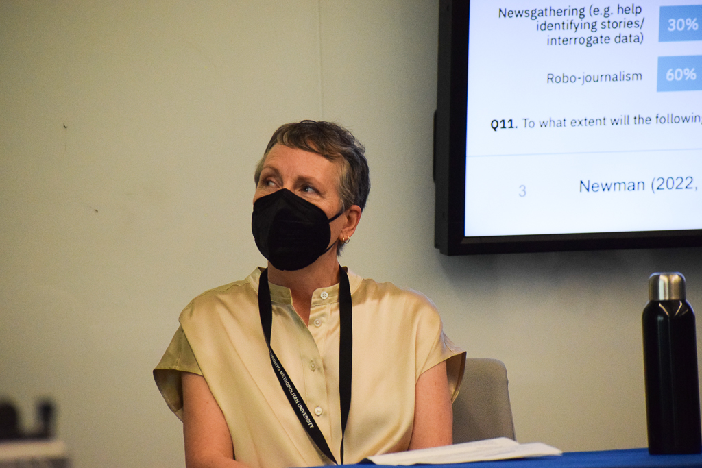 An a image of a white femme presenting individual with a pixie cut and a black KN95 mask looking to their left to something not visible in the photograph.