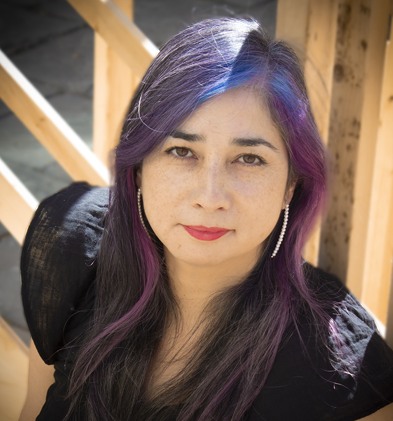 A photo of a person leaning against wooden boards with purple hair and pearl earrings.