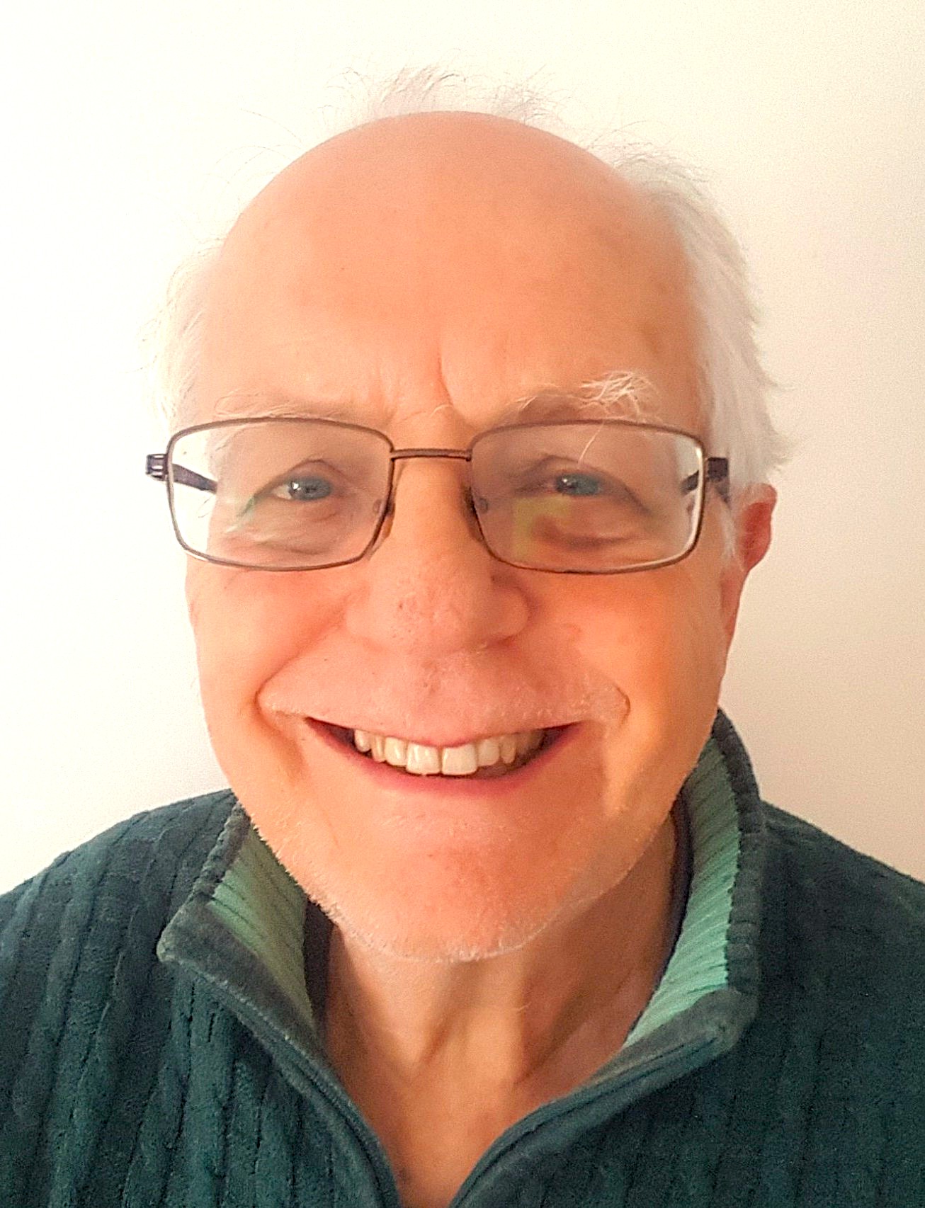 A photo of a person with white hair wearing eyeglasses and green jacket.