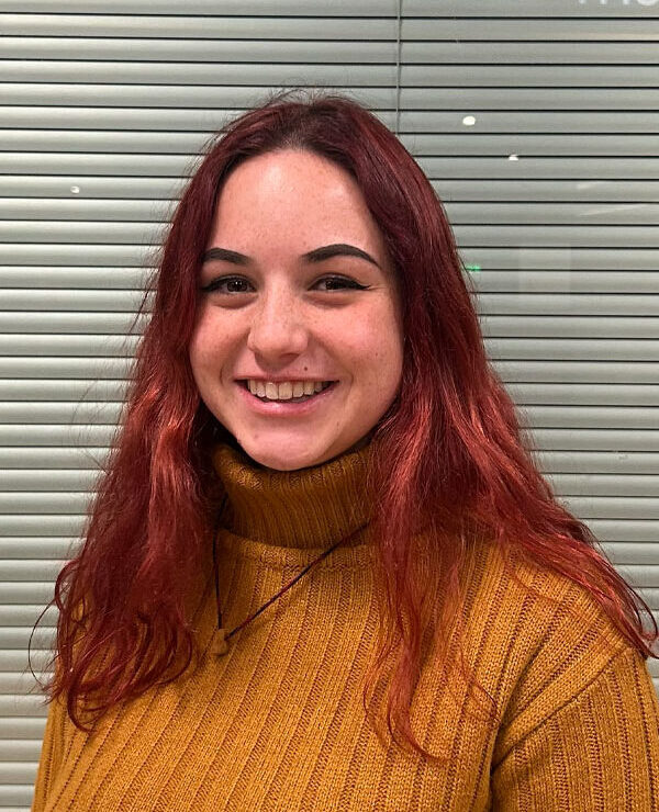 A person with long pink and brown hair wearing a yellow sweater.