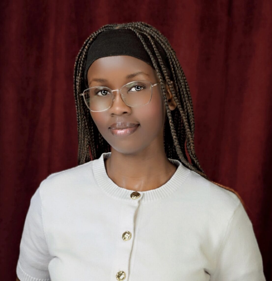 A person with long brown hair wearing a white shirt standing in front of a red background.